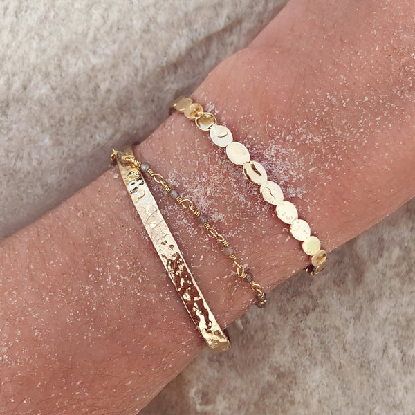 A female model’s wrist showcasing a layered look of multiple Kurafuchi gold bracelets and cuffs in various designs.