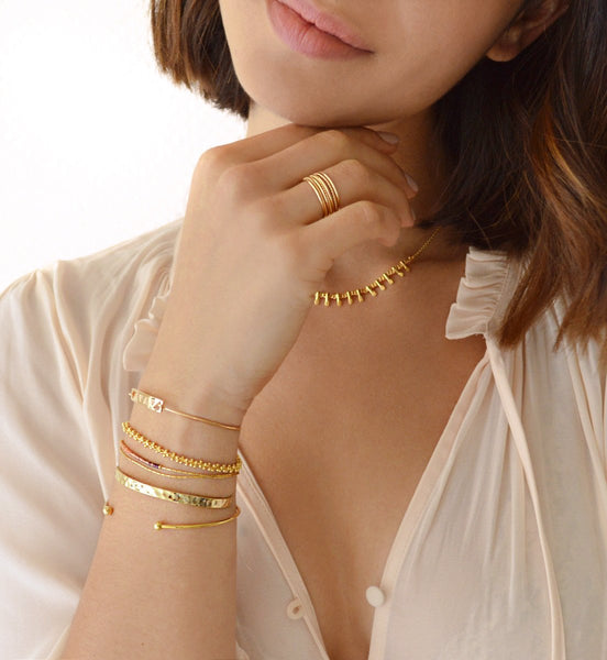 A female model’s wrist showcasing a layered look of multiple Kurafuchi gold bracelets in various designs and thicknesses.