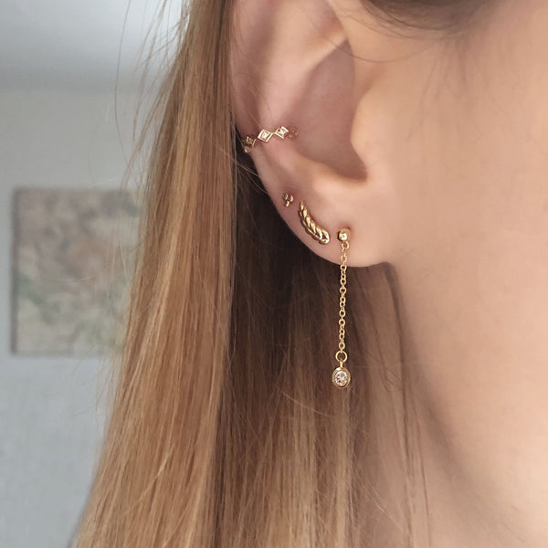A female model’s ear featuring several gold stud earrings and an ear cuff.