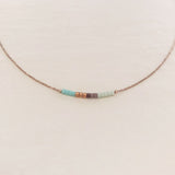 Minimalist necklace made of a dainty gold chain decorated with tiny beads in a colorful pattern. Designed by Kurafuchi.