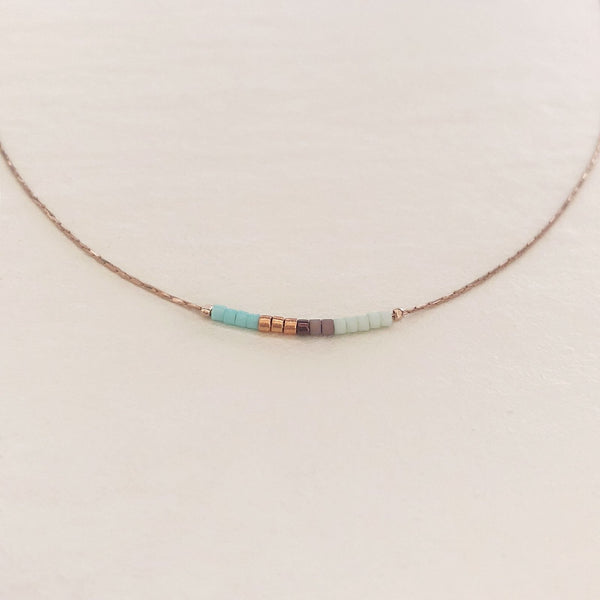 Minimalist necklace made of a dainty gold chain decorated with tiny beads in a colorful pattern. Designed by Kurafuchi.
