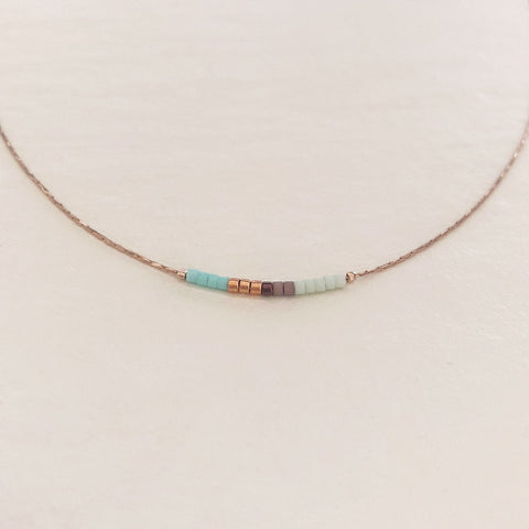 Minimalist necklace made of a dainty gold chain decorated with tiny beads in a colorful pattern. Designed by Kurafuchi.