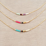 Minimalist necklace made of a dainty gold chain decorated with tiny beads in a colorful pattern. Designed by Kurafuchi.