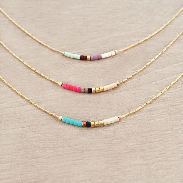 Minimalist necklace made of a dainty gold chain decorated with tiny beads in a colorful pattern. Designed by Kurafuchi.