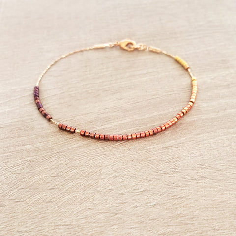 Dainty bracelet by Kurafuchi Jewelry, featuring a thin chain decorated with small beads in a gold to burgundy gradient.