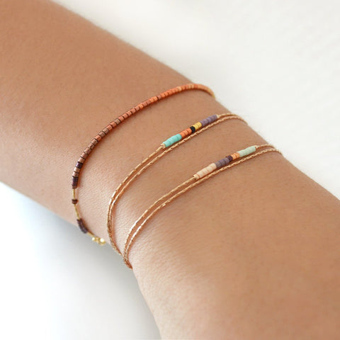 Dainty bracelet by Kurafuchi Jewelry, featuring a thin chain decorated with small beads in a gold to burgundy gradient.