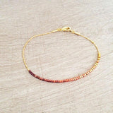 Dainty bracelet by Kurafuchi Jewelry, featuring a thin chain decorated with small beads in a gold to burgundy gradient.