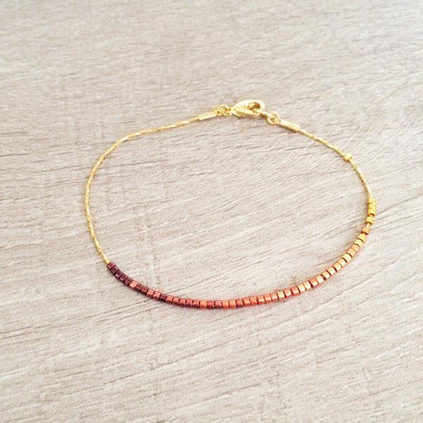 Dainty bracelet by Kurafuchi Jewelry, featuring a thin chain decorated with small beads in a gold to burgundy gradient.