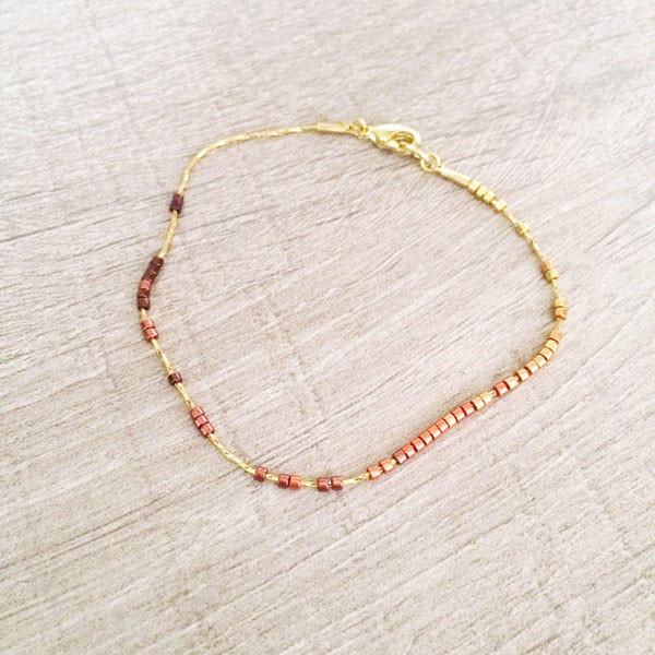 Dainty bracelet by Kurafuchi Jewelry, featuring a thin chain decorated with small beads in a gold to burgundy gradient.