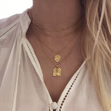 A female model wearing a layered look of gold pendant necklaces by Kurafuchi, some with medals.