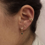 A female model’s ear featuring several gold stud earrings, hoops and ear cuffs.