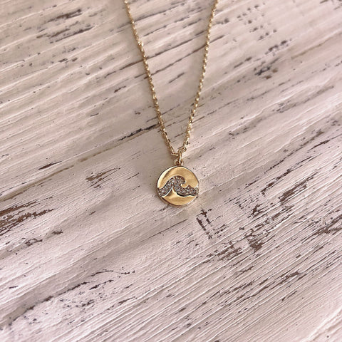 Pretty small pendant necklace with a tiny medal featuring a wave design made of tiny paved zircon crystals. By Kurafuchi.