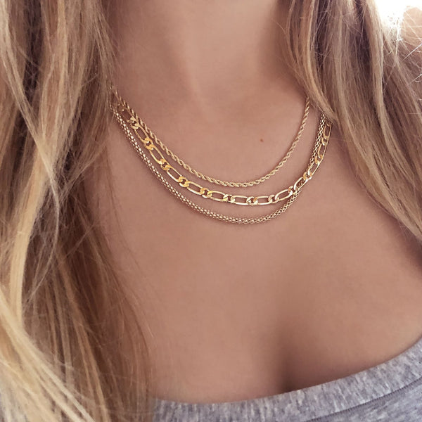 A female model wearing a layered look of gold chain necklaces by Kurafuchi Jewelry.