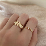 A female model’s hand featuring a stacked combination of various gold Kurafuchi rings over several fingers.