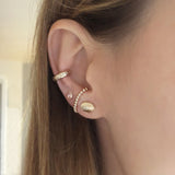 A female model’s ear featuring several Kurafuchi gold stud earrings, hoops and an ear cuff.