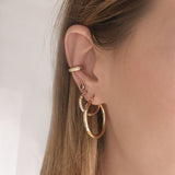 A female model’s ear featuring several Kurafuchi gold stud earrings, hoops and an ear cuff.