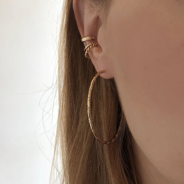 A female model’s ear featuring several Kurafuchi gold stud earrings, hoops and an ear cuff.