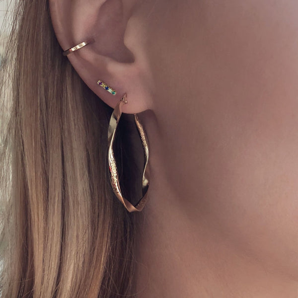 A female model’s ear featuring several gold stud earrings, hoops and an ear cuff.